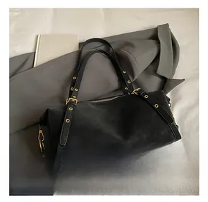 Detail view of black suede-texture pillow bag with gold eyelets and metallic buckle strap