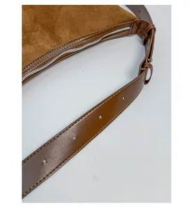 Detail of brown suede handbag with adjustable leather shoulder strap and silver zipper