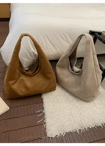 Détail de sacs hobo en daim en coloris caramel et beige sur un sol en bois