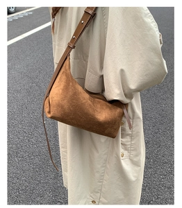 Detail of a brown suede hobo bag with silver buckle worn with a beige trench coat