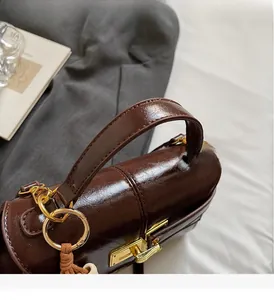 Detailed close-up of dark brown waxed leather bag with gold buckle and woven tassel detail