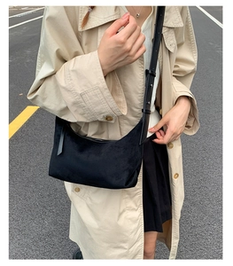 Detailed view of the black suede crescent shoulder bag worn with a beige trench coat
