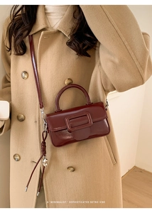 Close-up of burgundy retro patent leather bag with oversized buckle on tan coat