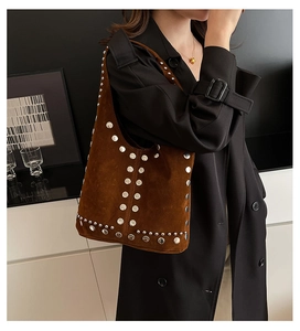 Sac sous le bras en daim marron orné de rivets argentés porté avec un manteau noir