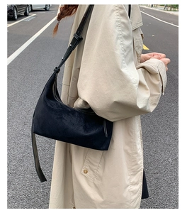 Close-up of black suede crescent bag with adjustable strap and zipper in street style
