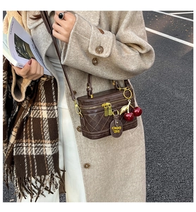 Detail of dark brown quilted box bag with cherry charm and gold metal zippers