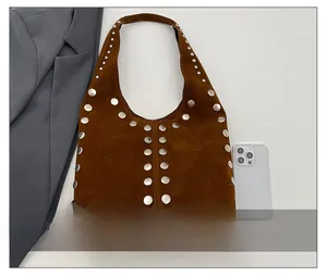 Dettaglio della borsa a spalla in camoscio marrone con borchie argentate e blazer