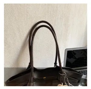 Detail of dark brown tote bag handle with golden hardware and fluffy pendant