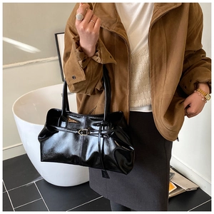 Detailed close-up of glossy black tote bag with metallic buckle and slim handles