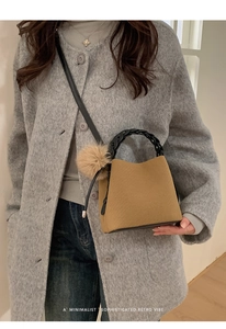 Detail of a retro ginger bucket bag with black woven handle and plush charm on grey coat