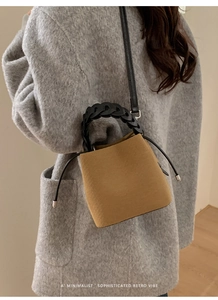 Detail of mustard yellow suede bucket bag with black woven handle on grey coat