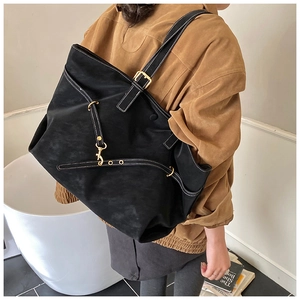 Detail of black tote bag with white contrast stitching and gold-toned metal buckles