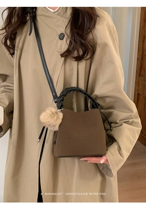 Close-up of retro brown suede bucket bag featuring woven handle and plush charm detail