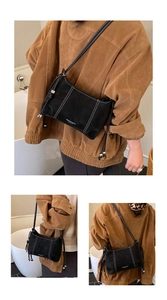 Detail of black suede shoulder bag with contrast white stitching and side tassels