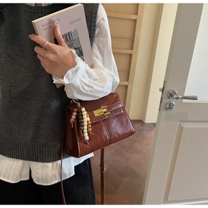 Detail of brown glossy leather crossbody bag with gold latch and colorful bead pendant