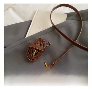 Detail of dark brown leather bag strap with golden metal hardware on a grey blazer