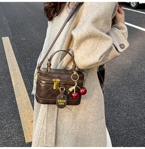 Deep brown box handbag with quilted pattern and cherry charm worn with a beige coat