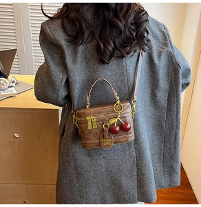 Detail of vintage brown quilted box bag with cherry pendant shown on shoulder
