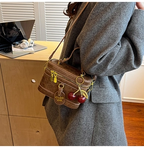 Detail of vintage brown textured box bag with gold zippers and a red cherry charm