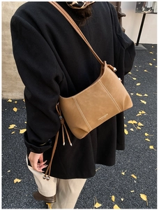 Close-up of khaki leather crossbody bag with white contrast stitching and tassel details