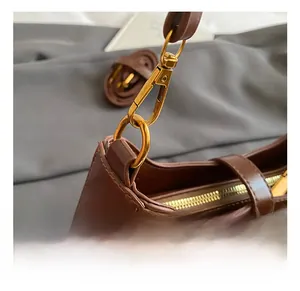 Detail shot of the golden metal hook and brown leather shoulder strap connection