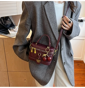 Quilted burgundy box handbag with cherry charm shown on model in stylish office setting