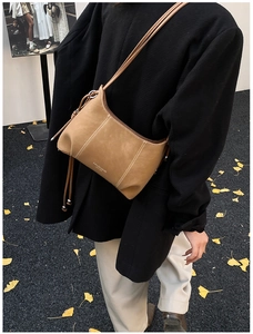 Detail of camel leather crossbody bag with decorative side drawstring and metal pendant