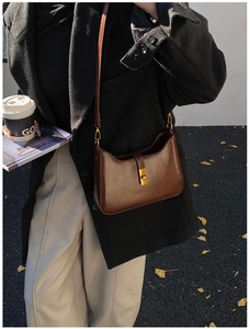 Street style view of a dark brown leather underarm bag with a gold square clasp on black coat
