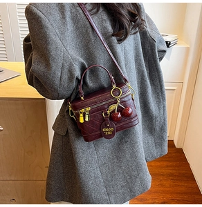 Detail of burgundy box bag with quilted pattern, golden hardware and cherry pendant