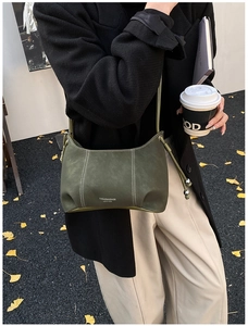 Detail of dark green matte leather bag with white stitching and drawstring on street backdrop