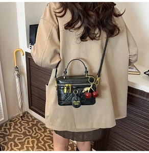 Detail of black quilted box bag with gold hardware and a decorative cherry charm