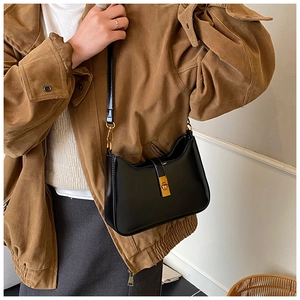 Close-up of a black minimalist underarm bag with a gold rectangular buckle on a model