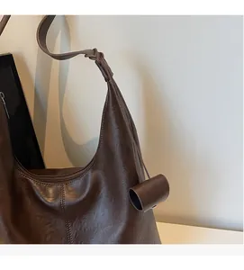 Detail view of large brown hobo bag with pebble texture and cylinder charm