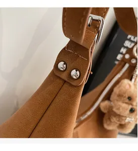 Detailed close-up of brown leather bag featuring silver metal rivets and bear charm