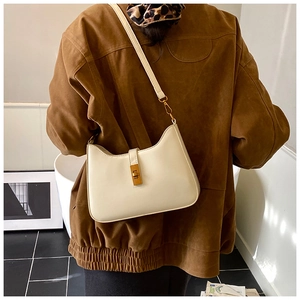 Close-up of cream leather shoulder bag with gold square twist lock on brown suede jacket
