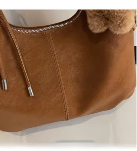 Close-up of brown faux leather shoulder bag with fine stitching and plush pompom detail