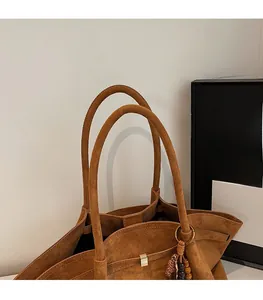 Detail of brown suede tote bag featuring slim cylindrical straps and a metal magnetic clasp