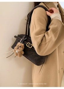 Detail of dark brown retro shoulder bag with golden buckle and plush bear charm decoration