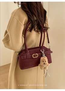 Detail of burgundy leather shoulder bag featuring golden buckle and plush puppy charm