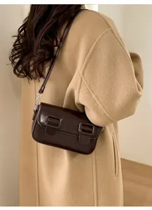 Detail van donkerbruine rechthoekige crossbodytas met dubbele gespen op wollen jas