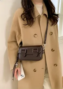 Detailopname van een donkerbruine glanzende crossbodytas met chique vierkante gespen