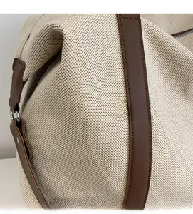 Detail aus cremefarbenem Canvas-Stoff und braunem Ledergriff mit Metallring-Schnalle