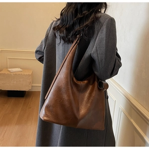 Detail of a large brown faux leather tote bag with vertical stitching on a grey coat