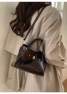 Detail of dark brown glossy leather tote bag with mini charm on a beige trench coat