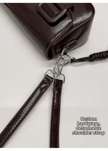 Detail van zilveren hardware en afneembare riem op bruine glanzende leren vierkante tas