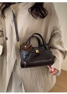 Detail of dark brown polished leather bag with suede charm on beige trench coat
