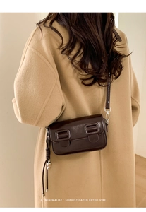 Detail van retro donkerbruine glanzende crossbodytas met hartjeshanger op een camel jas