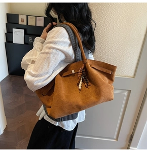 Detail view of large brown suede tote bag with fringe charm on shoulder