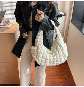 Gros plan sur la texture du sac hobo matelassé beige porté avec un manteau noir