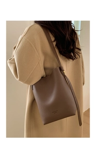 Detailed view of the dark brown lychee leather texture and gold buckle on bucket bag